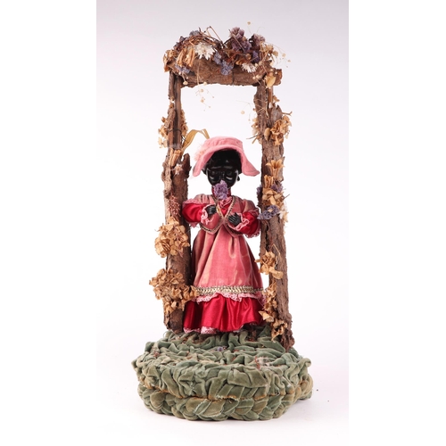 1564 - A Victorian style automaton black doll in Victorian dress standing beneath a floral arch, under a gl... 