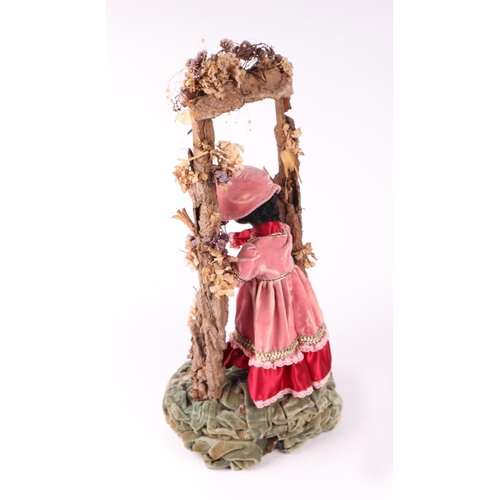 1564 - A Victorian style automaton black doll in Victorian dress standing beneath a floral arch, under a gl... 