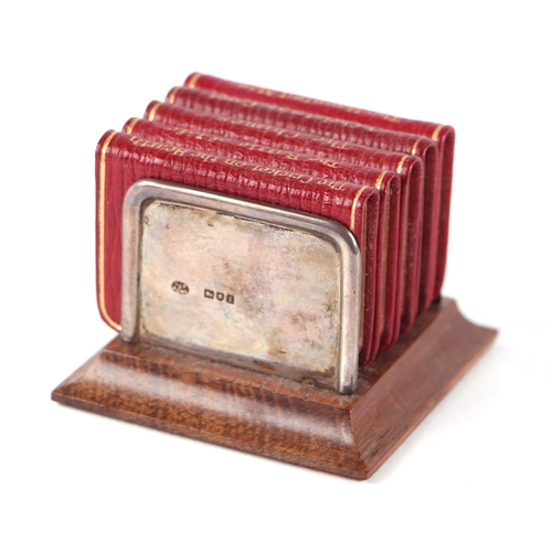 404 - A set of Charles Dickens miniature books on a silver and oak stand, 6.5cms wide.