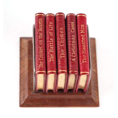 404 - A set of Charles Dickens miniature books on a silver and oak stand, 6.5cms wide.