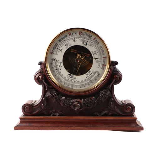 879 - An Edwardian aneroid barometer in a gilt metal case, 20cms diameter, mounted in a carved mahogany st... 