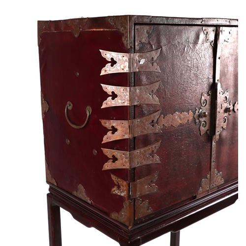 631 - A Chinese leather covered trunk with copper reinforced strap work, the twin doors opening to reveal ... 