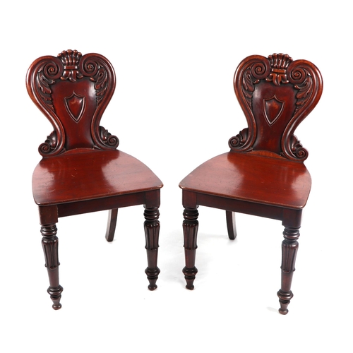 1083 - A pair of Victorian mahogany hall chairs with carved backs and central shield shaped blank cartouche... 