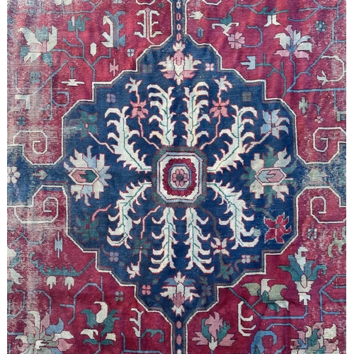 158 - A large Persian carpet, the central blue medallion on a red ground within a repeating floral pattern... 