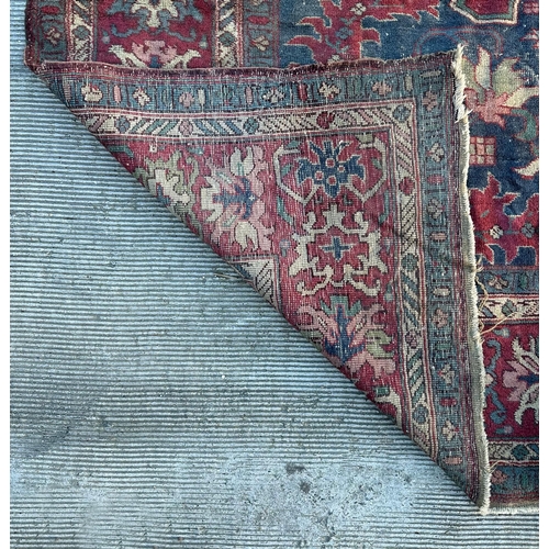 158 - A large Persian carpet, the central blue medallion on a red ground within a repeating floral pattern... 