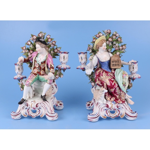 309 - A pair of continental porcelain figural candlesticks depicting a young lady and gentleman seated on ... 