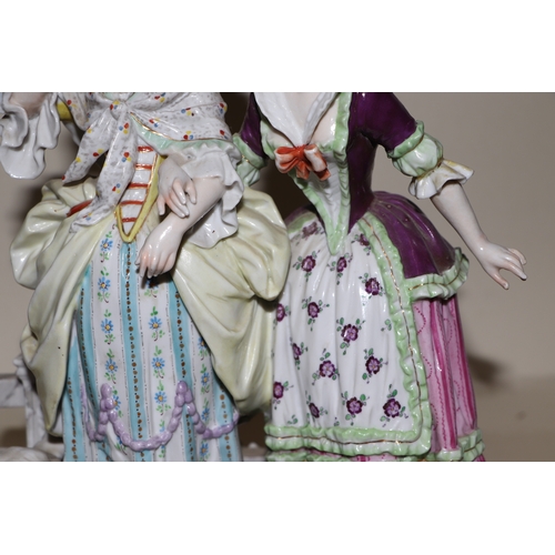 286 - A continental porcelain group depicting two ladies standing by a gate with a spaniel dog, 26cms high... 