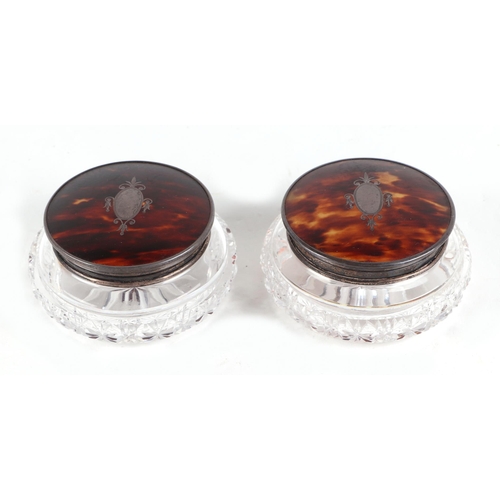 497 - A pair of George V glass cosmetic jars with tortoiseshell and silver lids, each 11cm wide (2)