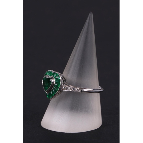 539 - A platinum ring set with a heart shaped emerald, surround by calibre cut emeralds and diamond set sh... 