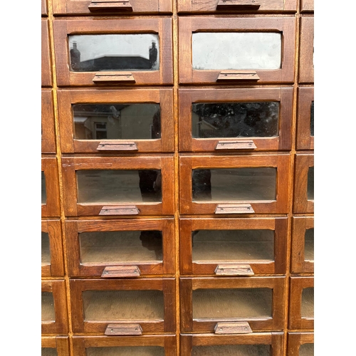 832 - A mid century substantial haberdashery cabinet, with sixty oak fronted glazed drawers, above three l... 