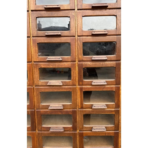 832 - A mid century substantial haberdashery cabinet, with sixty oak fronted glazed drawers, above three l... 