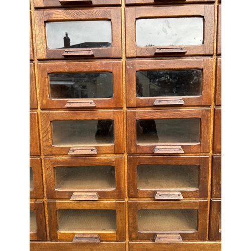 832 - A mid century substantial haberdashery cabinet, with sixty oak fronted glazed drawers, above three l... 