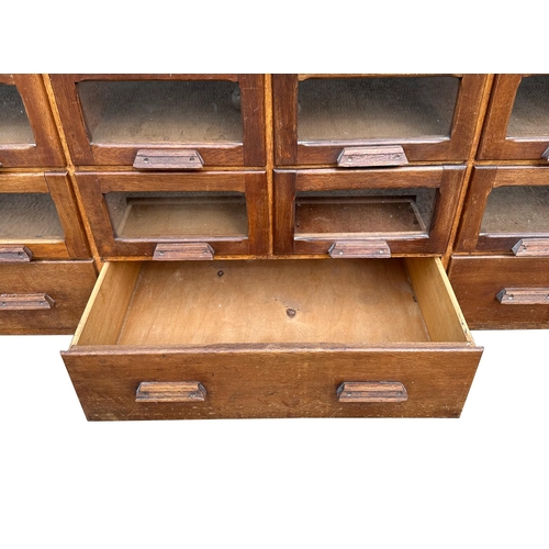 832 - A mid century substantial haberdashery cabinet, with sixty oak fronted glazed drawers, above three l... 