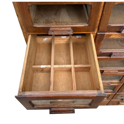 832 - A mid century substantial haberdashery cabinet, with sixty oak fronted glazed drawers, above three l... 