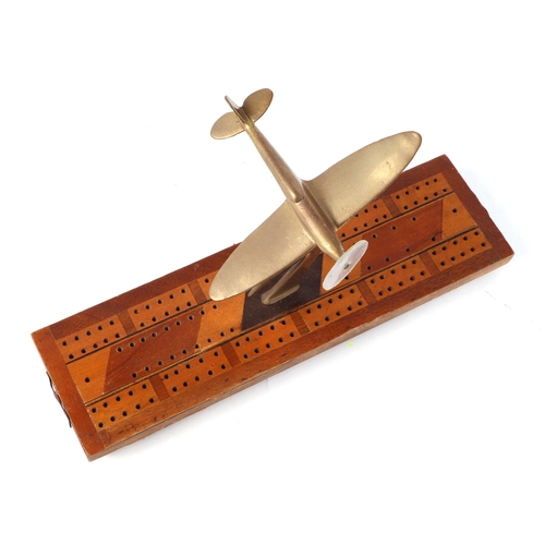 36 - A trench art cast brass model of a Spitfire aircraft, mounted on a cribbage board, wingspan 13cm.