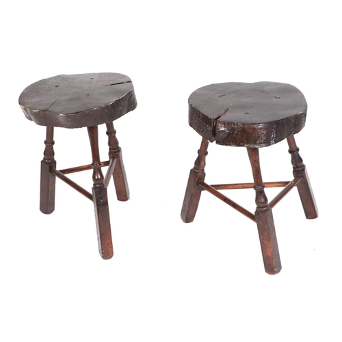 706 - A near pair of primitive tripod stools with sawn solid elm seats on turned supports joined by stretc... 