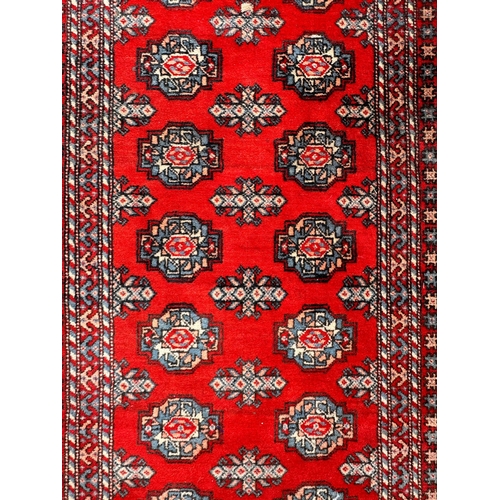 81 - A large Persian Turkoman runner with repeating guls and geometric motifs, on a red ground within a m... 