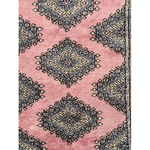 89 - A Persian Bokhara hand knotted woollen rug with four central guls within borders, on a pink ground, ... 