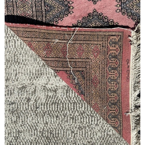 89 - A Persian Bokhara hand knotted woollen rug with four central guls within borders, on a pink ground, ... 