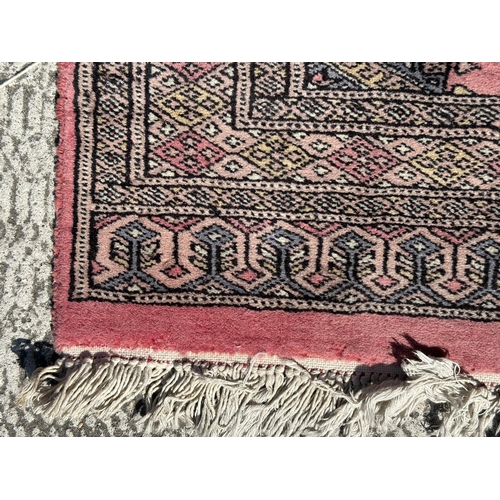 89 - A Persian Bokhara hand knotted woollen rug with four central guls within borders, on a pink ground, ... 