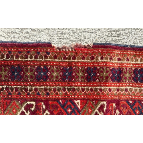 95 - A Persian Balouch hand knotted woollen rug with all over geometric design, on a red ground, 95 by 55... 