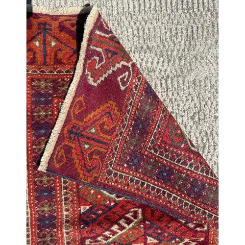 95 - A Persian Balouch hand knotted woollen rug with all over geometric design, on a red ground, 95 by 55... 