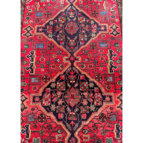 96 - A Persian Koliai hand knotted woollen rug with geometric designs, on a red ground, 154 by 240cms.