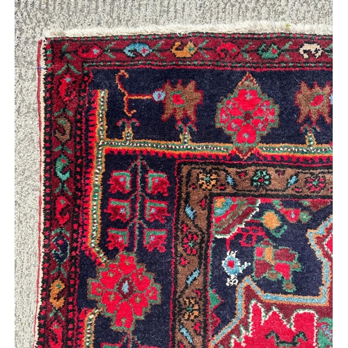 96 - A Persian Koliai hand knotted woollen rug with geometric designs, on a red ground, 154 by 240cms.