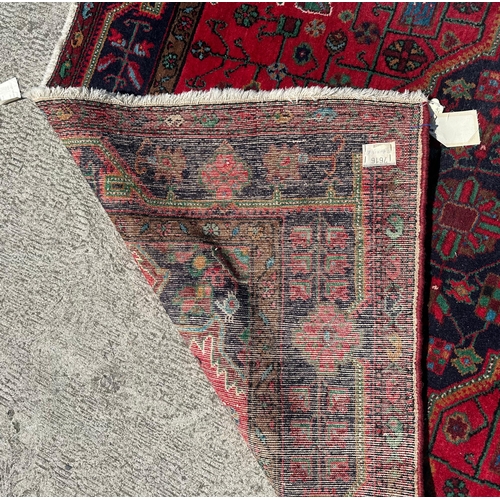 96 - A Persian Koliai hand knotted woollen rug with geometric designs, on a red ground, 154 by 240cms.