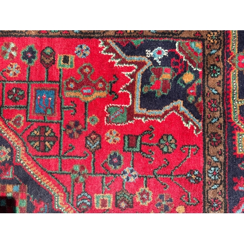 96 - A Persian Koliai hand knotted woollen rug with geometric designs, on a red ground, 154 by 240cms.