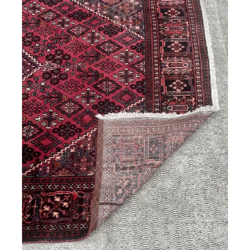 100 - A Persian hand knotted Shiraz carpet with central stylised gul within repeating borders, on a red gr... 