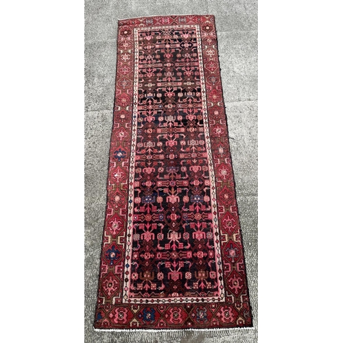 106 - A Persian Hamadan runner with repeating stylised floral design, on a red ground, 290 by 105cms.