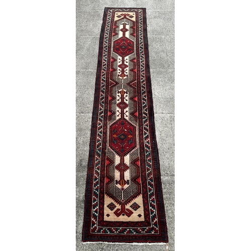 113 - A Persian hand knotted Qashqai runner with two red lozenges within a repeating stylised design, on a... 