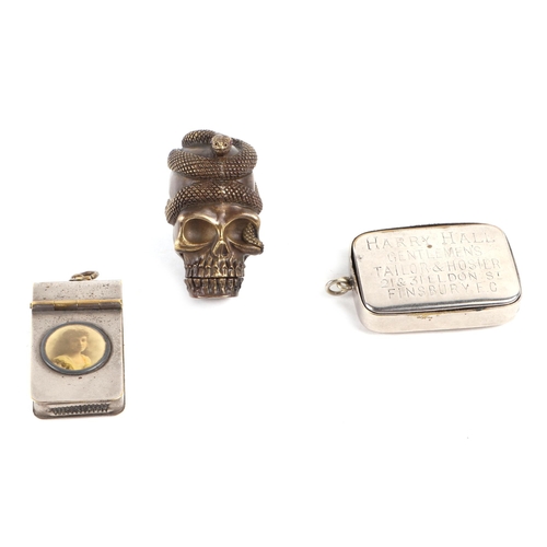 395 - Three vesta cases comprising a brass example in the form of a skull wrapped with a snake; a WWI era ... 