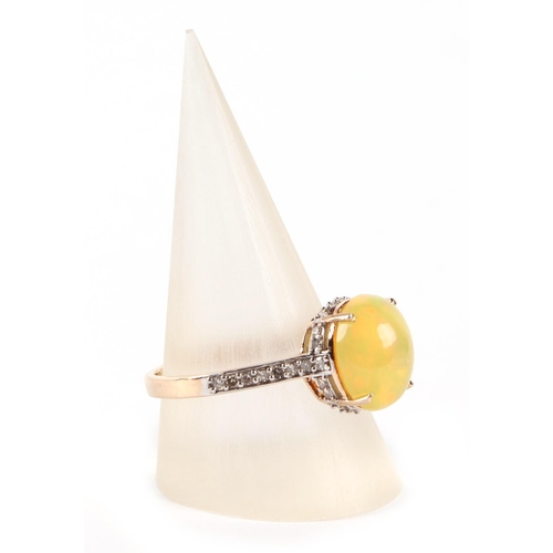 611 - A 9ct gold ring set with an oval yellow opal cabochon surrounded by diamonds and diamond set shoulde... 