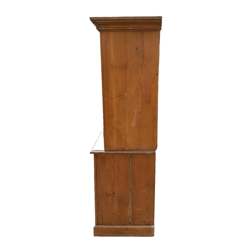 901 - A pine glazed cupboard on chest, the pair of glazed doors enclosing a shelved interior above two lon... 