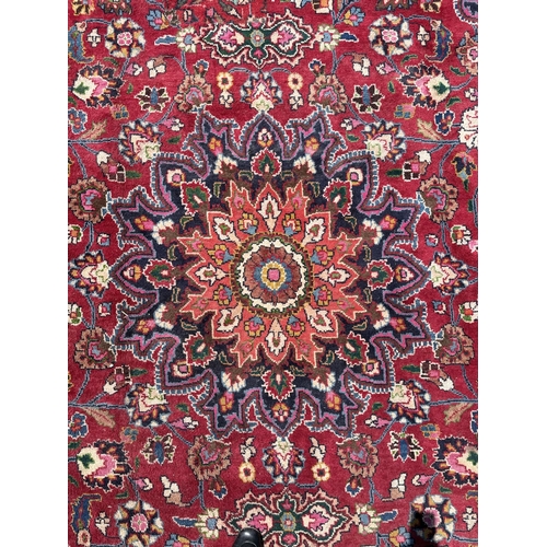 51 - A Persian Meshed carpet with central rosette medallion and floral borders, on a red ground, 390 by 2... 