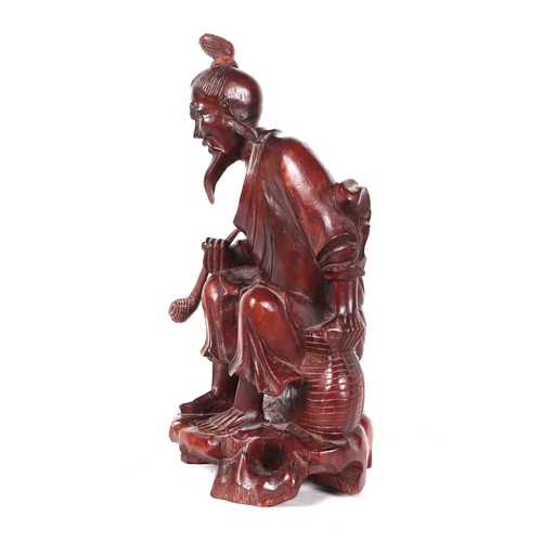 519 - A Chinese hardwood figure depicting a bearded man holding a pipe seated beside a basket, 26cms high.