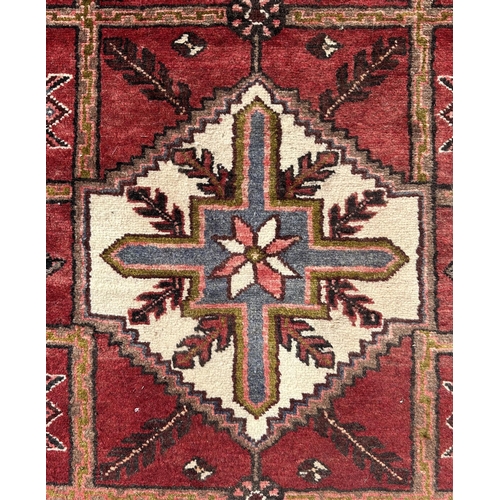 61 - A Persian hand knotted woollen Hamadan runner with three central ivory medallions on a tiled red gro... 