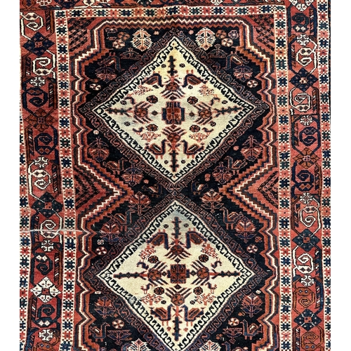 133 - A Persian Shiraz rug with two central medallions, on a pale red ground, 92 by 127cms.