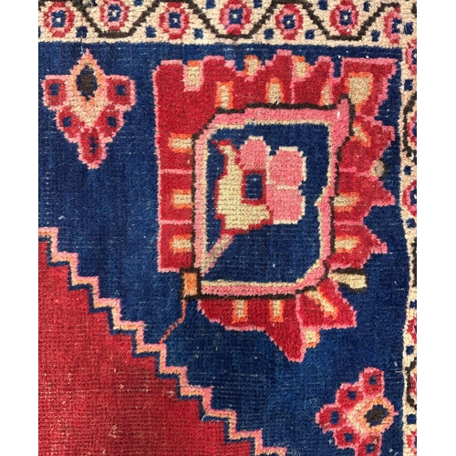 141 - A Persian Baluch runner with central floral medallion and blue spandrels, on a red ground, 95 by 220... 