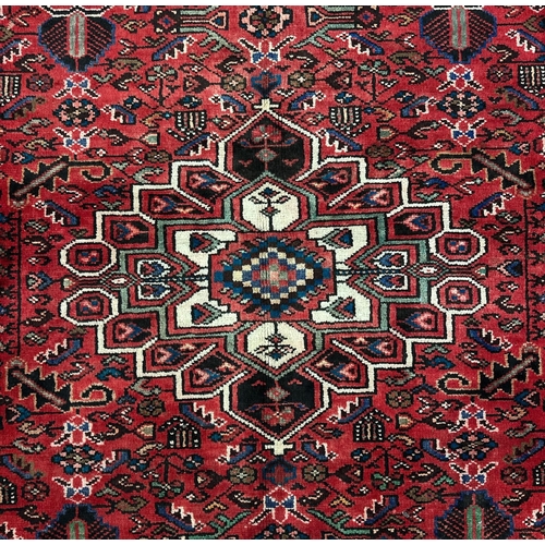 148 - A Persian hand knotted woollen Hamadan rug with central medallion within floral borders, on a red gr... 