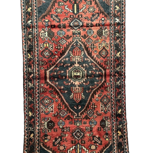 150 - Persian Hamedan hand knotted woollen runner with central gul within a stylised design, on a red grou... 