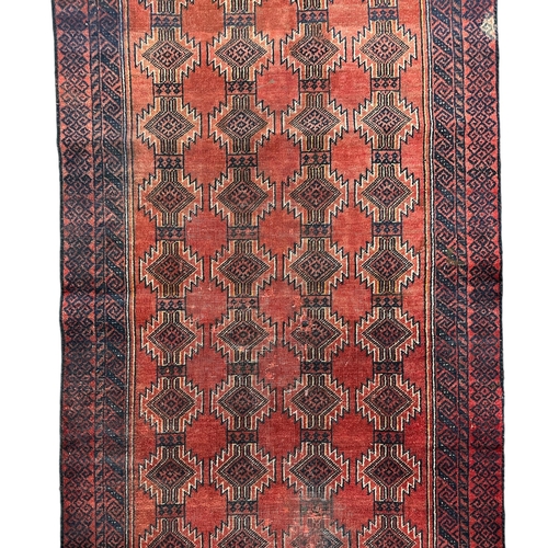 152 - A Persian Balouch woollen hand knotted rug with repeating guls within stylised borders, on a red gro... 