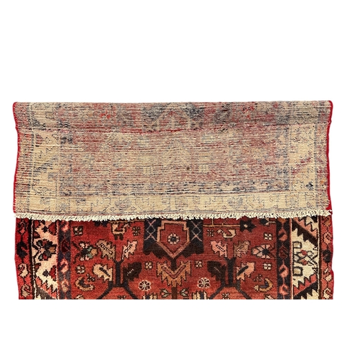 157 - A Persian Hamadan hand knotted woollen rug with repeating stylised design, on a red ground, 105 by 1... 