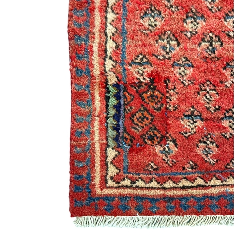 158 - A Persian Arak hand knotted woollen rug with repeating boteh design, on a red ground, 97 by 177cms.