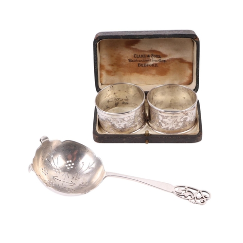 420 - A pair of silver napkin rings; together with a pierced silver tea strainer, 68g (3).