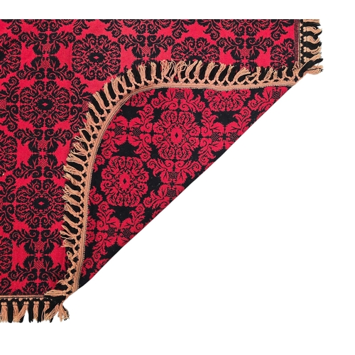 701 - A Welsh woollen throw or wall hanging with repeating black motifs on a red ground, 240 by 200cms.