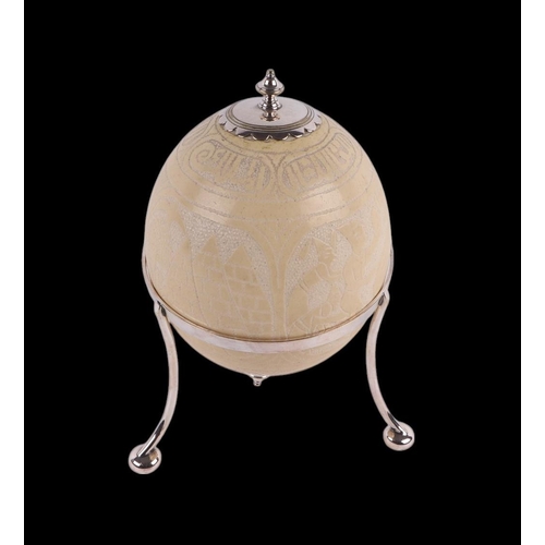 919 - A carved ostrich egg on a silver plated tripod stand, decorated Islamic script approx 23cms high.