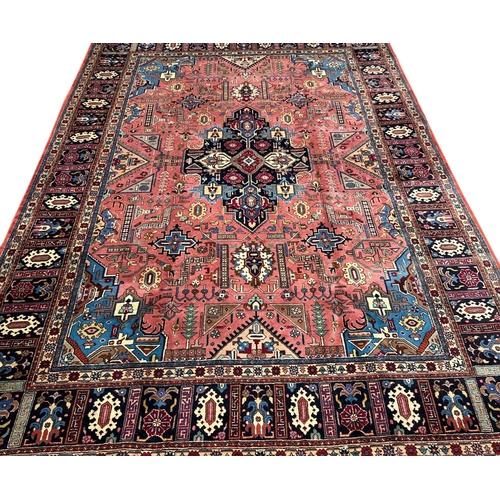 135 - A Persian Heriz woollen hand knotted carpet with stylised floral central medallion on a pink ground ... 